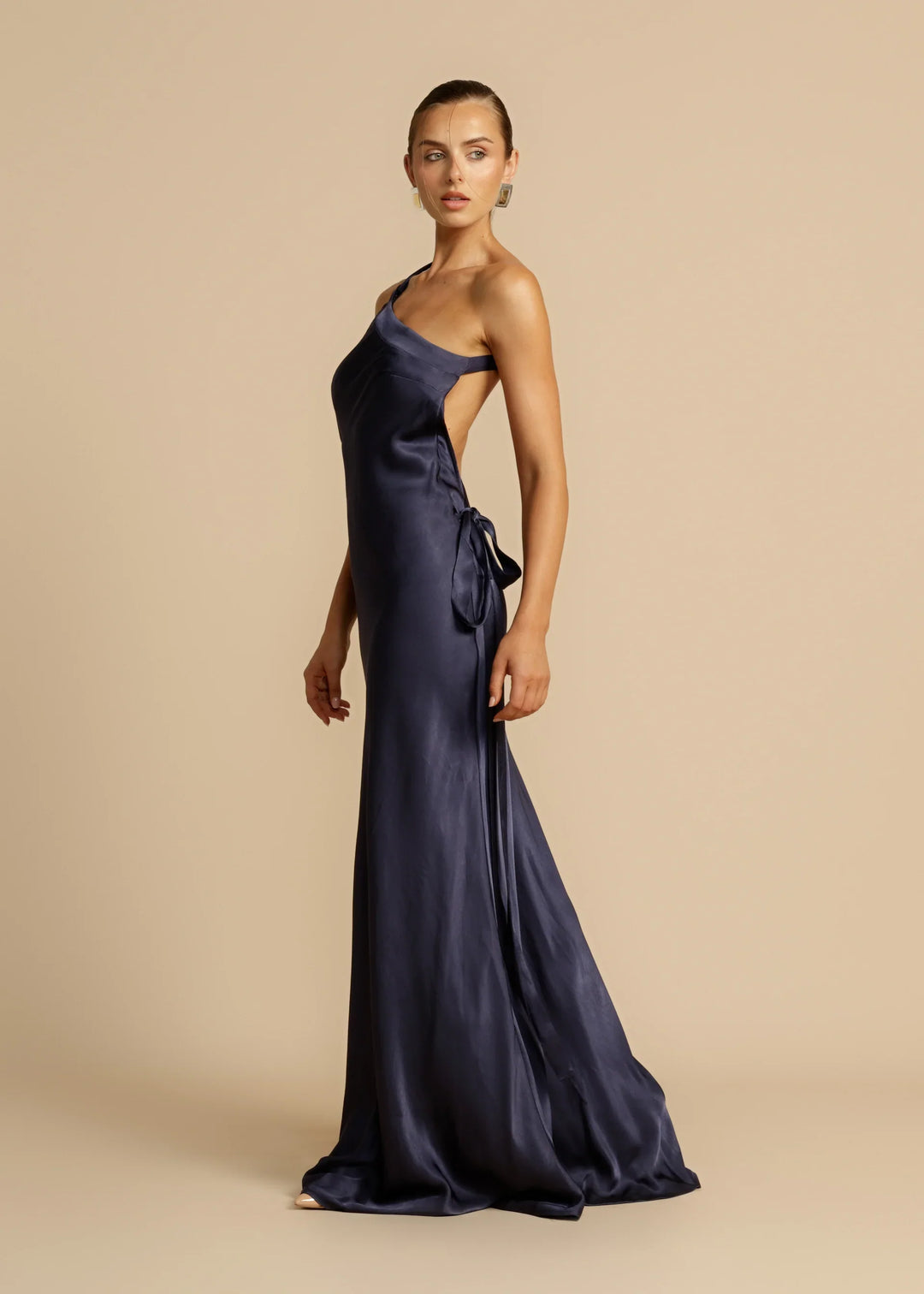Woman wearing a navy one-shoulder gown on a beige background