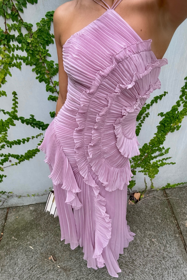 Person wearing a pink ruffled dress standing against a white wall with greenery.