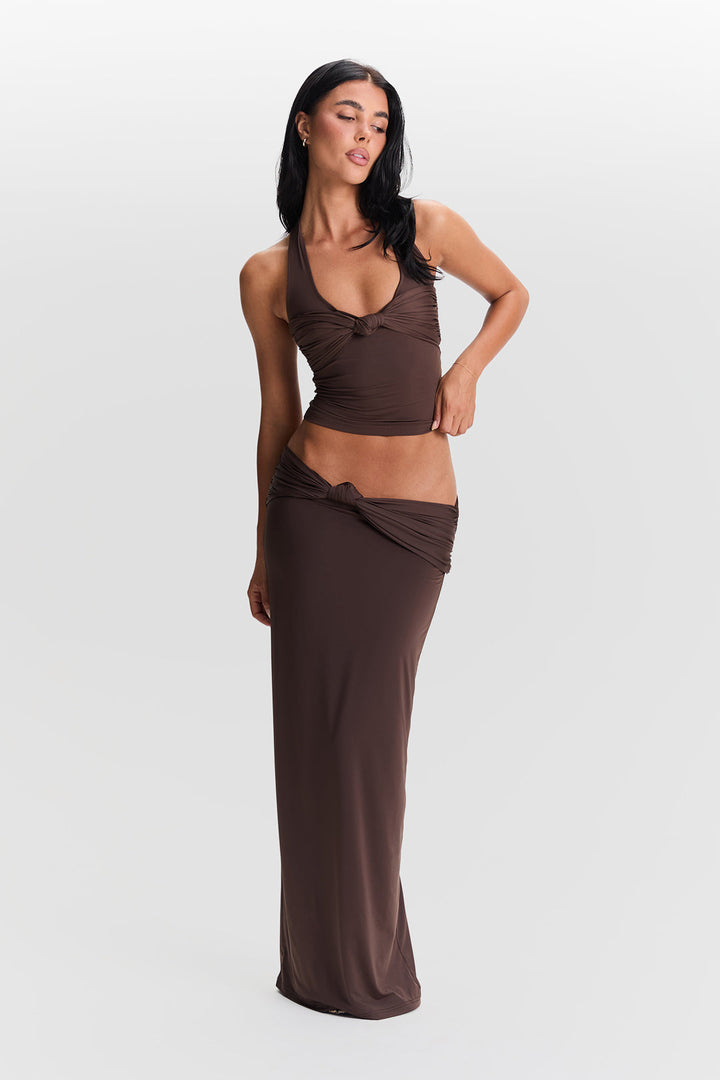 Woman wearing a brown halter top and long skirt on a white background