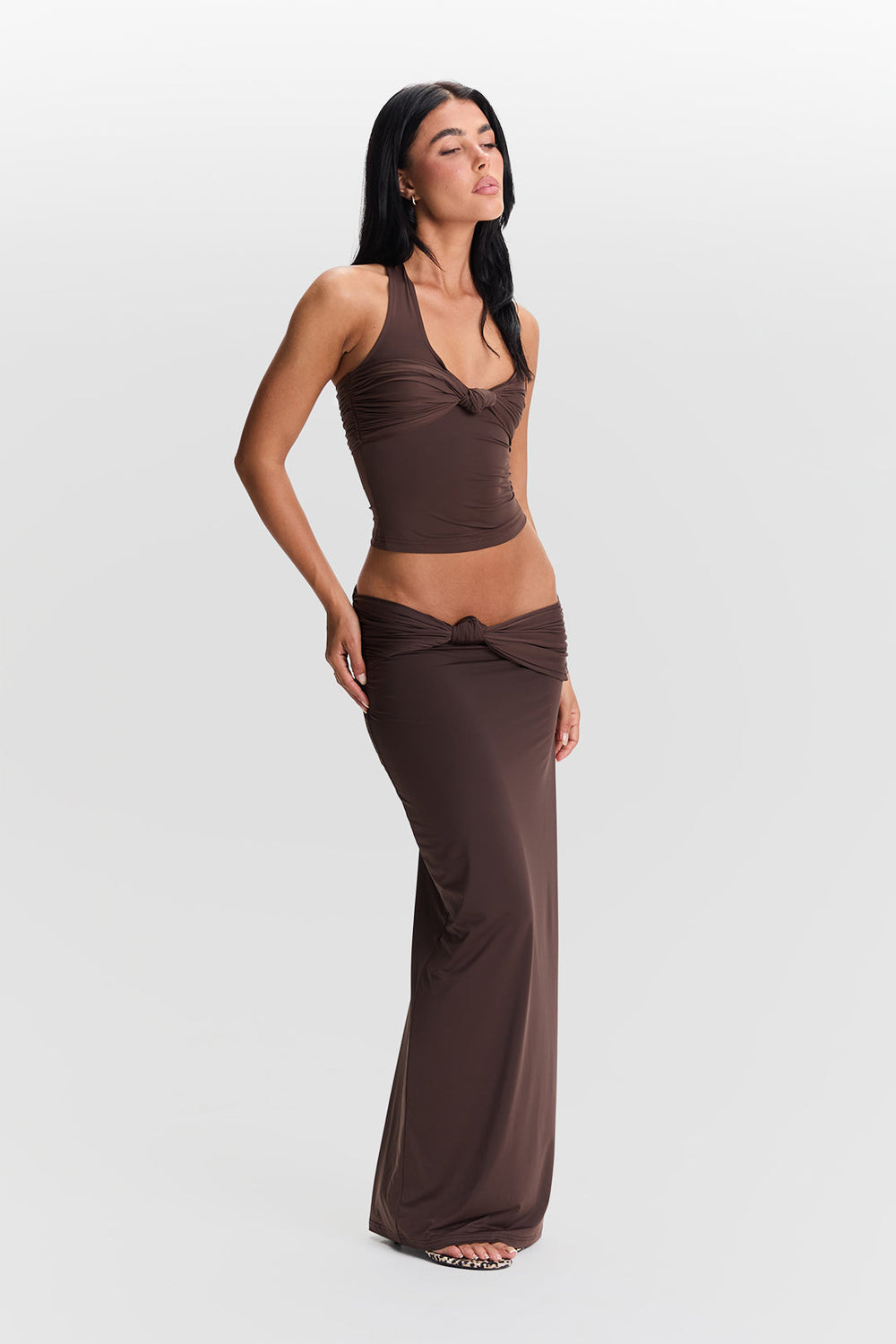 Woman wearing a brown sleeveless top and long skirt on a white background