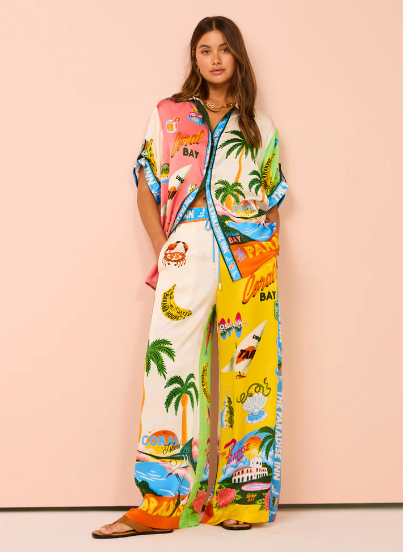 Woman wearing a colorful tropical-themed outfit with a matching jacket against a pink background