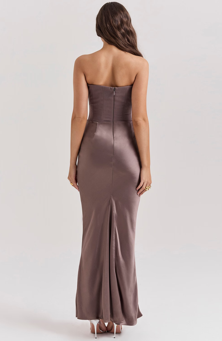 Woman wearing a strapless, floor-length dress with a slit on a plain background