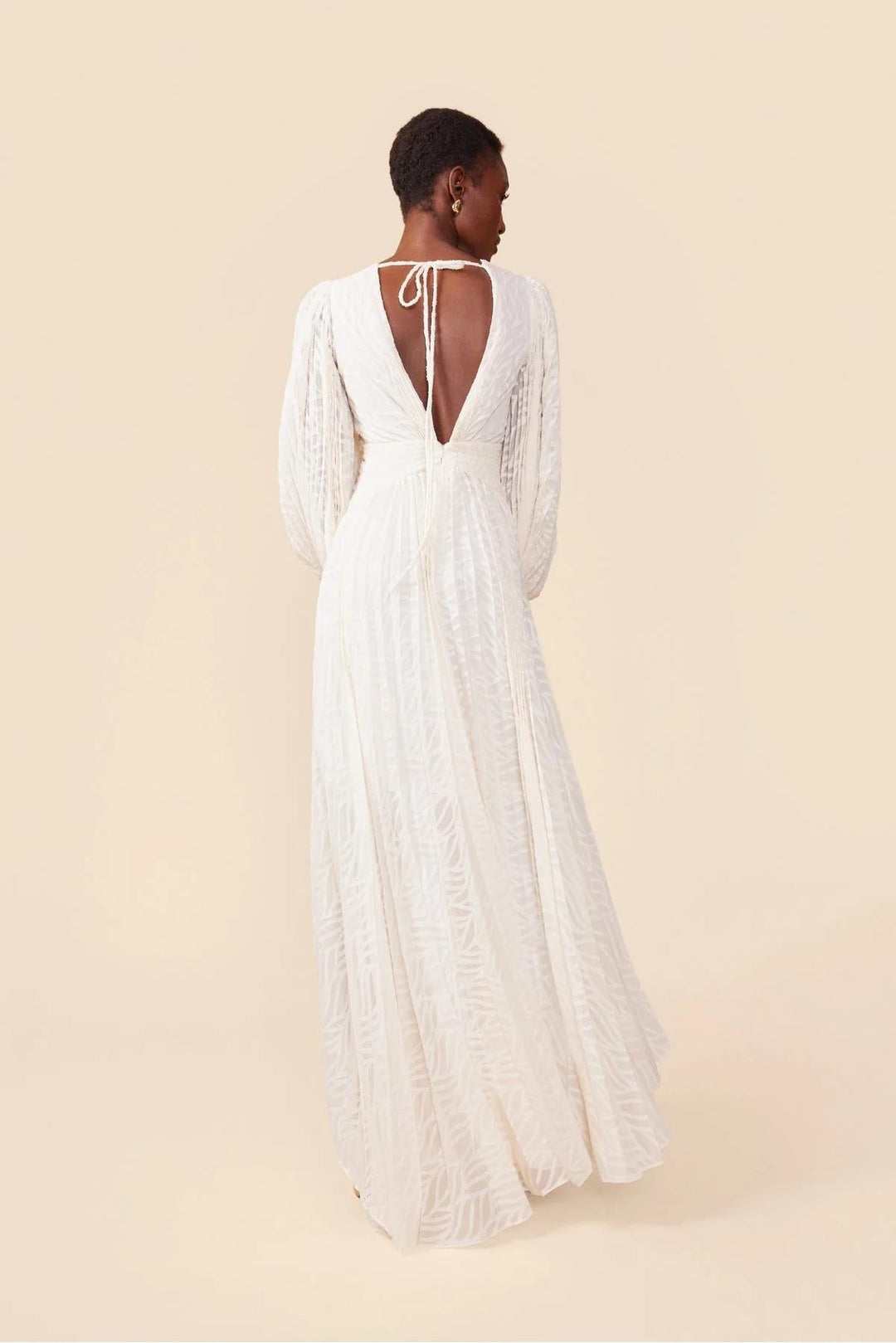 Woman wearing a white lace dress with long sleeves on a beige background