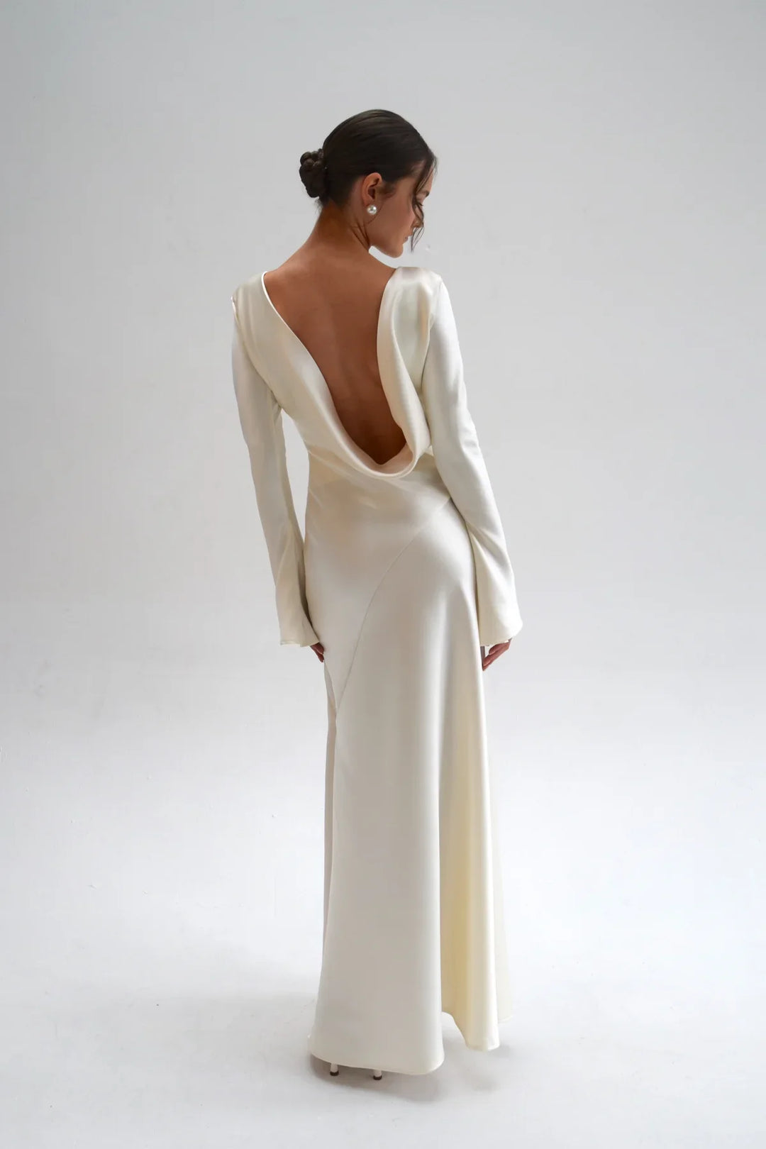 Woman wearing a white gown with a low back on a plain background