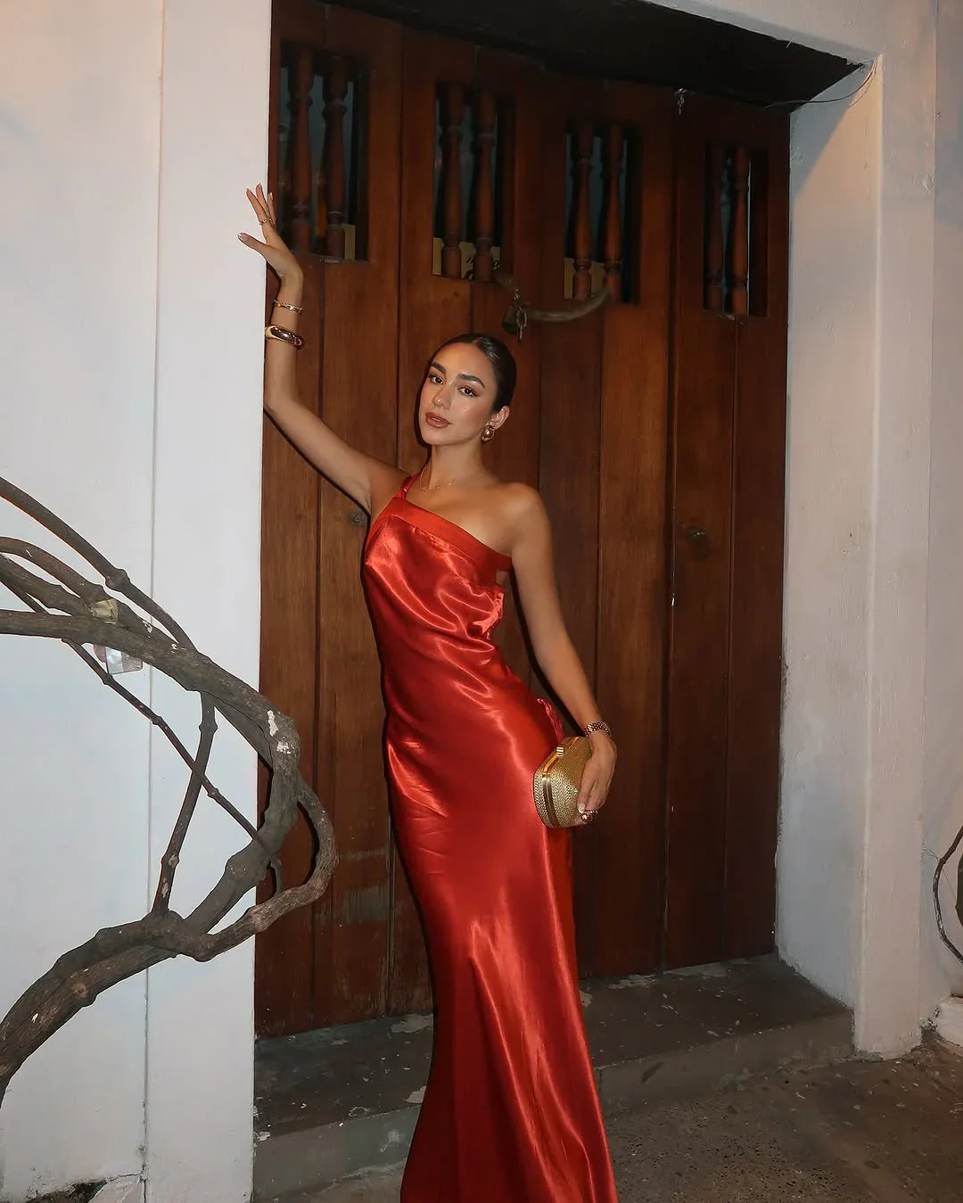 Woman in a red dress holding a gold clutch against a wooden door.