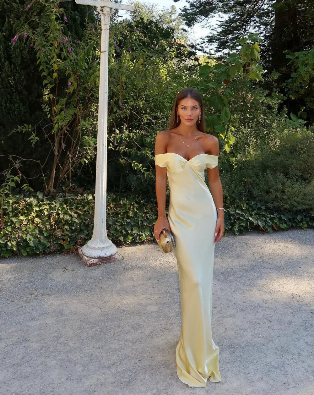 Woman in a yellow evening gown standing outdoors with greenery in the background