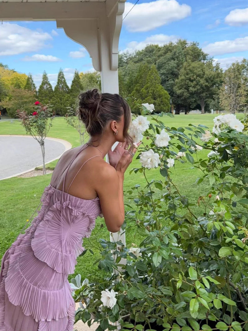 Woman in a purple dress smelling flowers in a garden with a gazebo and pond in the background.
