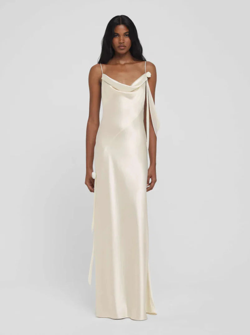 A female model wearing a beige satin dress with a cowl neckline and spaghetti straps.