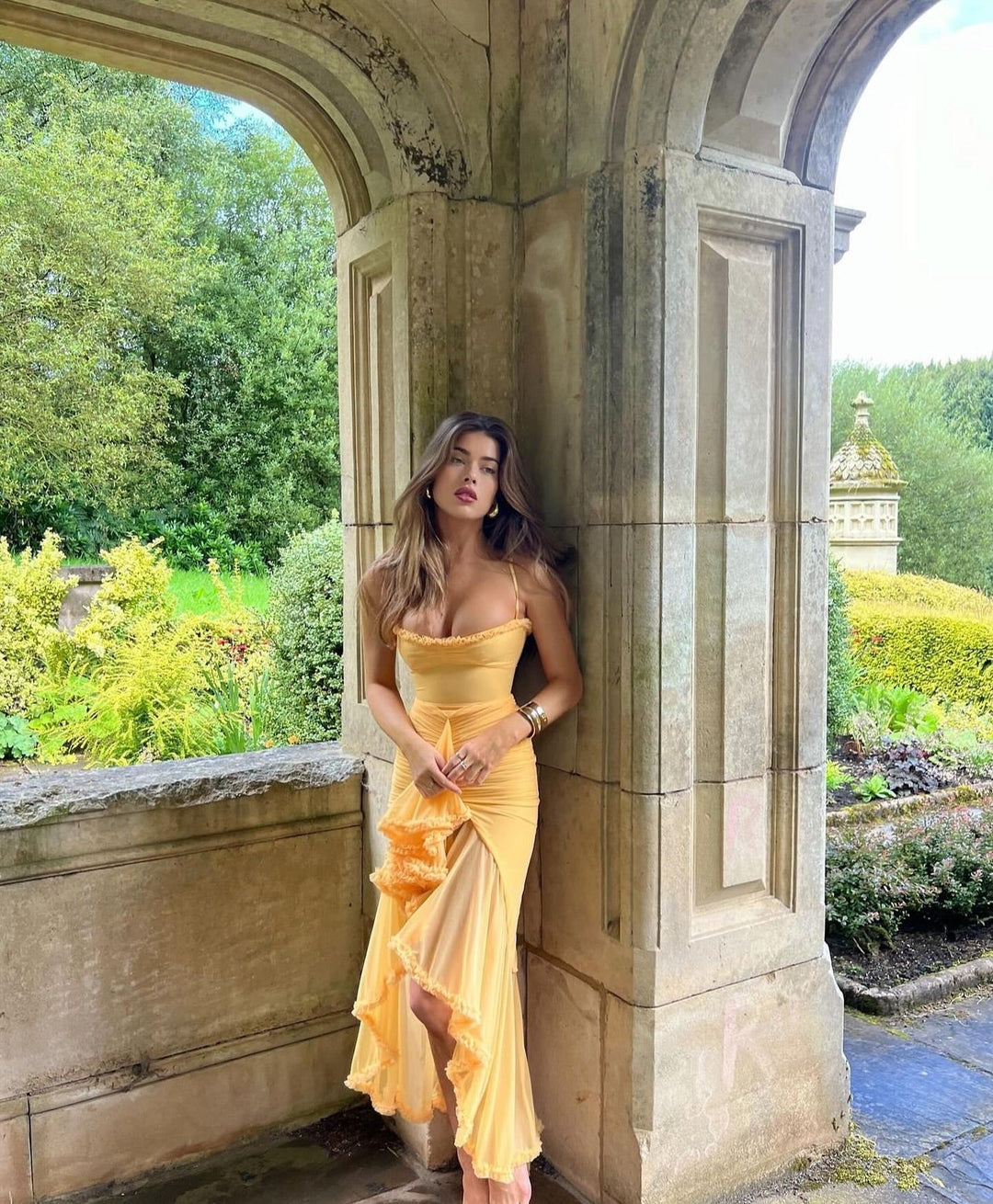 Woman in a yellow dress standing in an archway with garden scenery