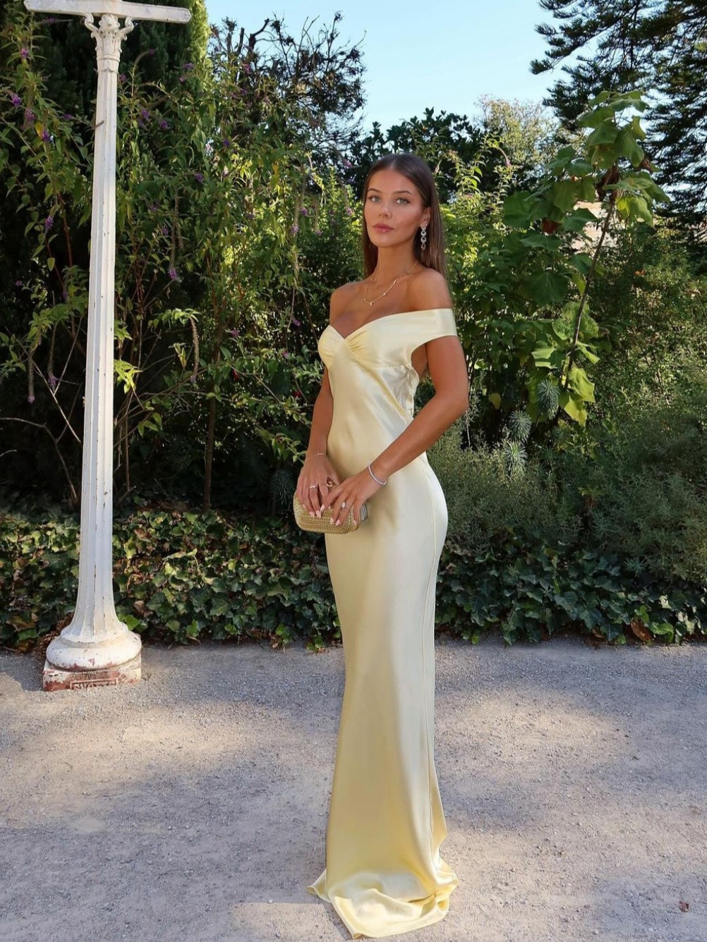 Woman in a yellow off-shoulder dress standing outdoors with greenery in the background