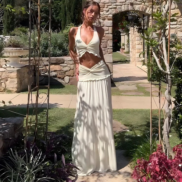 Woman in a white dress standing in a garden with stone archway and plants.