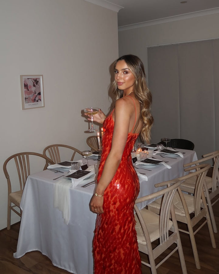 Woman in a red dress standing in a dining room with tables and chairs.