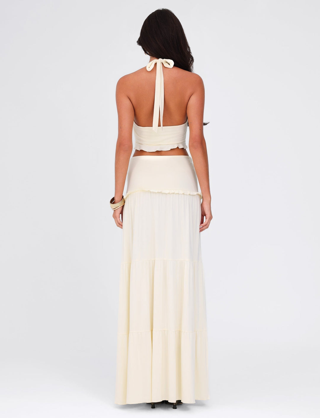 Woman wearing a white halter top and long skirt set on a light gray background