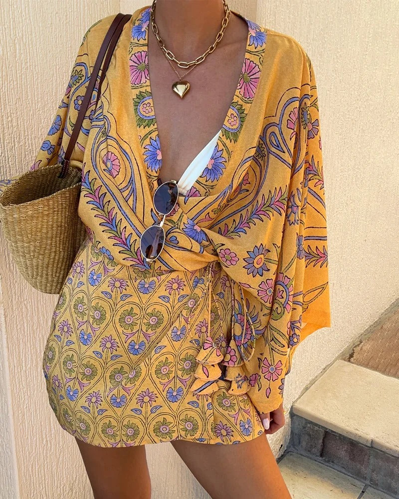 Person wearing a yellow patterned outfit with sunglasses and a bag, standing against a beige wall.