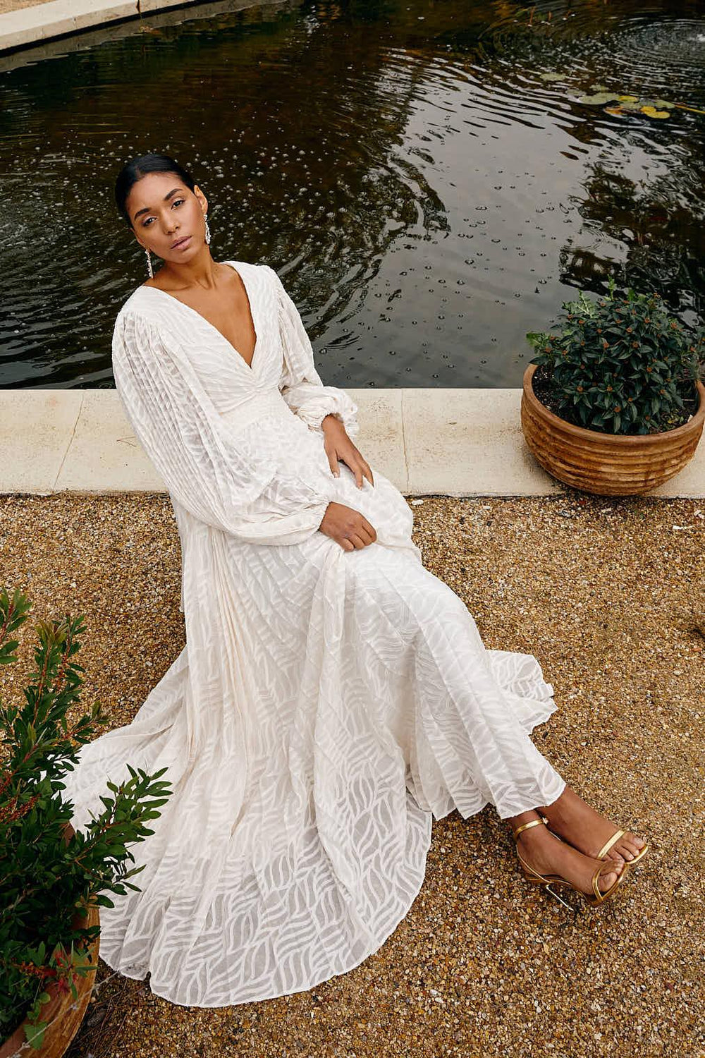 Woman in a white dress sitting by a pond with plants around