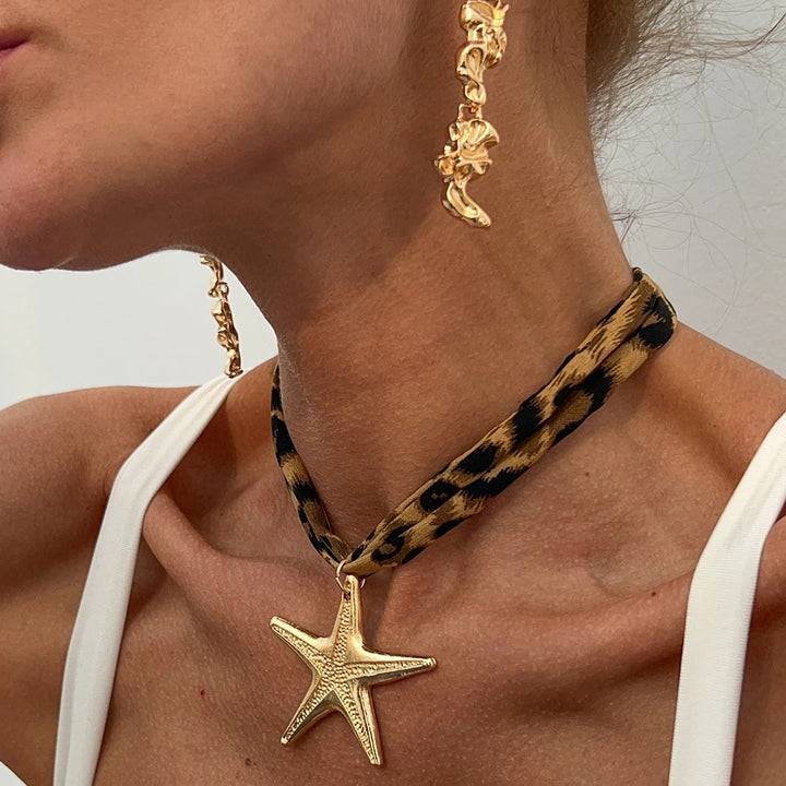 Close-up of a person wearing a gold starfish pendant necklace with a leopard print strap.