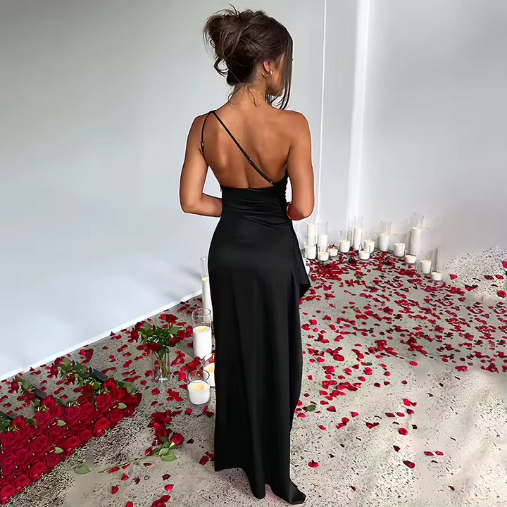 Woman in a black dress standing in a room with red rose petals and candles.