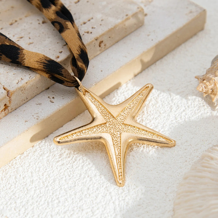 Gold starfish pendant on a leopard print cord with seashells in the background