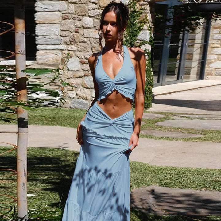 Woman in a blue dress standing outdoors with a stone wall and grass in the background