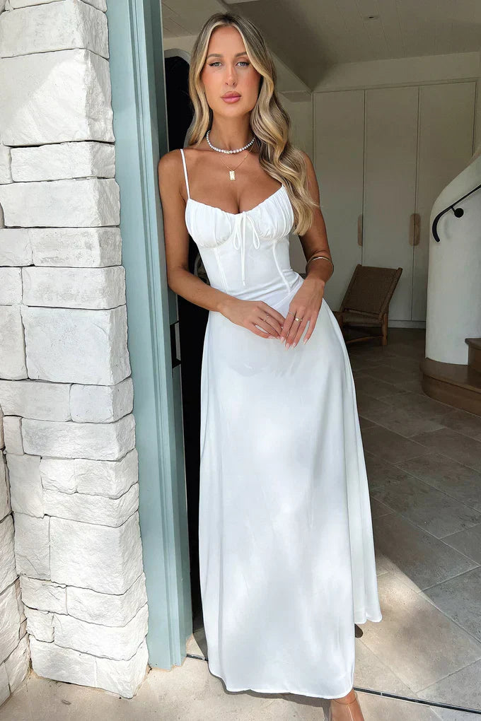 Woman in a white dress standing by a stone wall indoors.