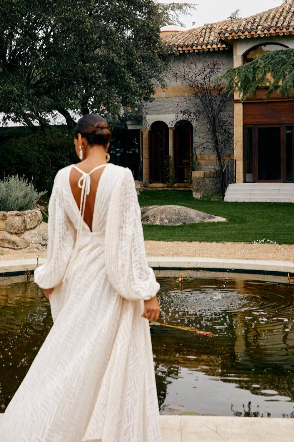 Woman in a white dress standing by a pool with a scenic background