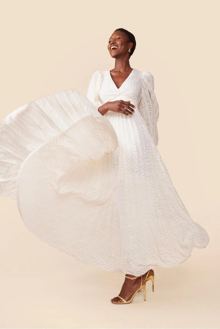 Woman wearing a flowing white dress against a beige background