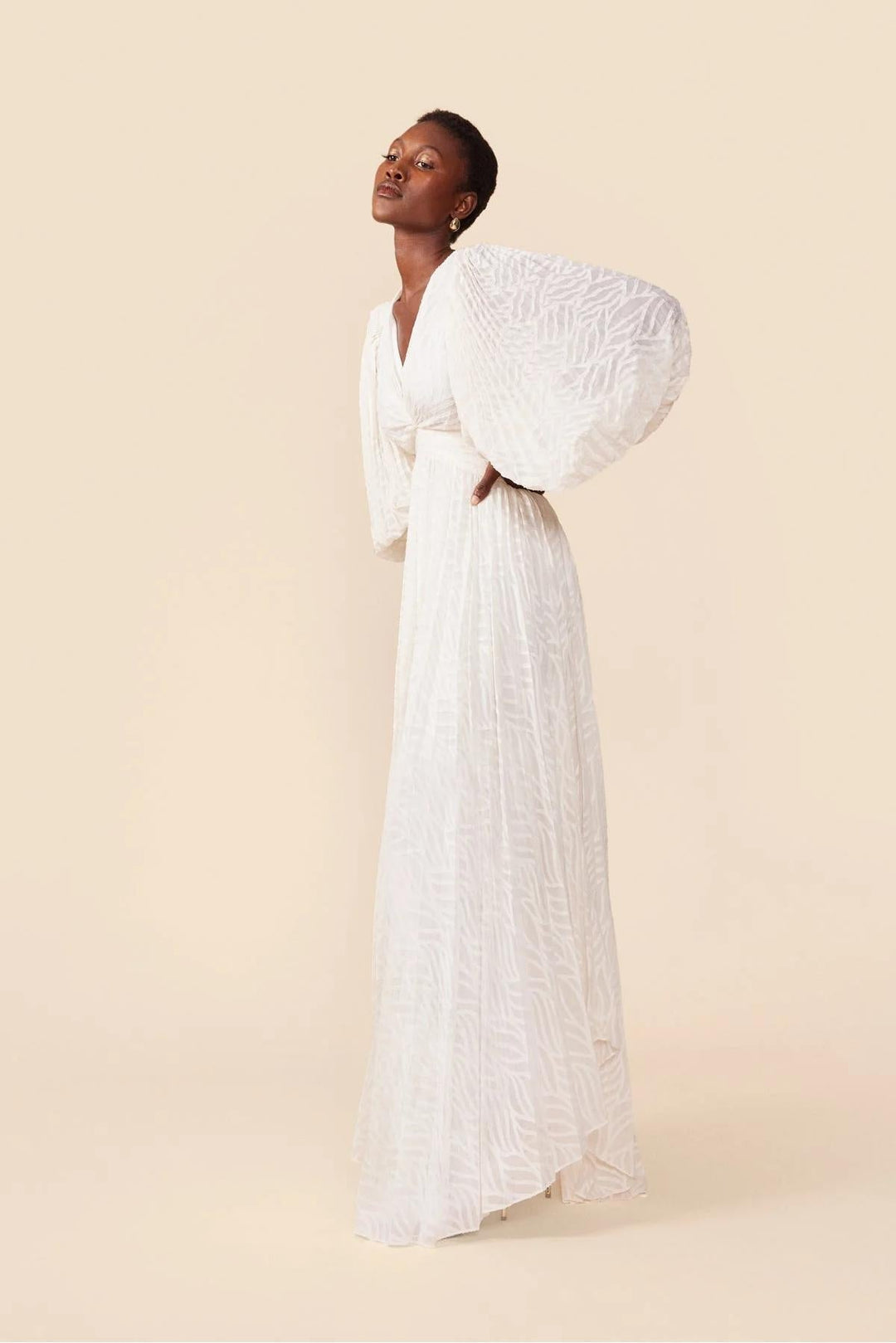 Woman wearing a white dress with puffed sleeves against a beige background