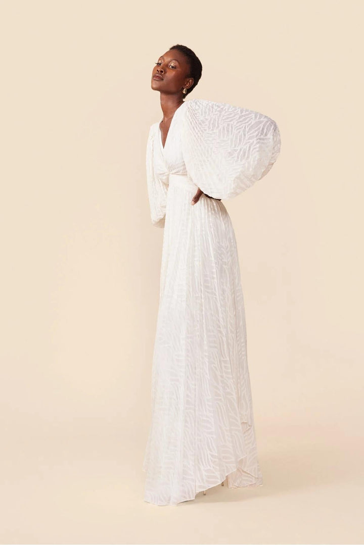 Woman wearing a white dress with puffed sleeves against a beige background